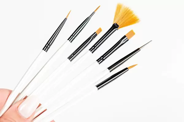 Frau hält mehrere Make-Up Pinsel in der Hand. Weißer Hintergrund