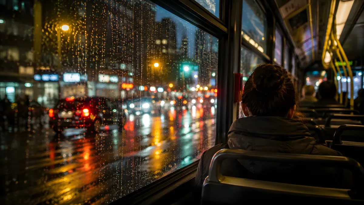 Frau im Bus blickt durch regennasse Scheibe bei Nacht