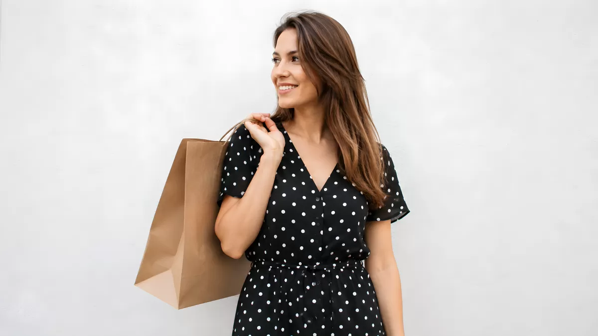 Frau im Polka-Dot-Kleid trägt Einkaufstasche lächelnd