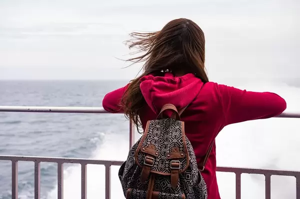 Frau im roten Pullover und Rücksack mit Blick aufs Meer