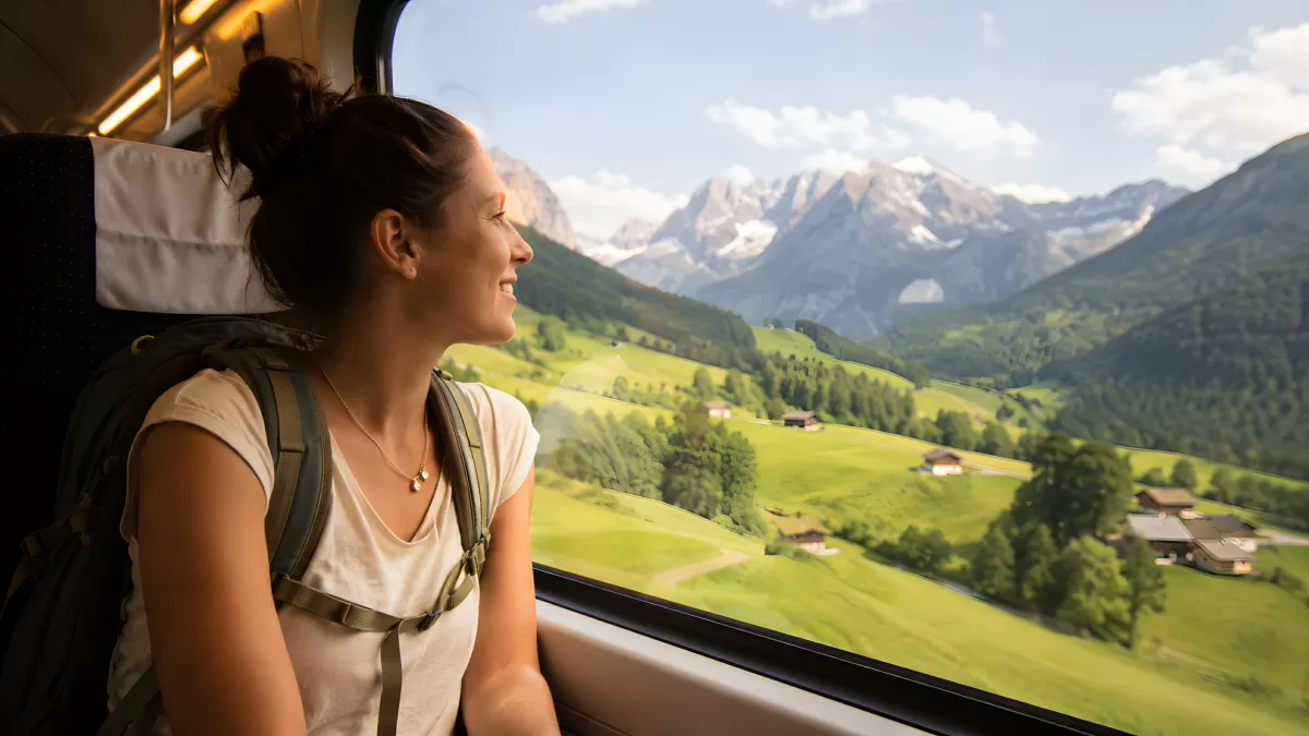 Frau im Zug blickt auf Alpenlandschaft