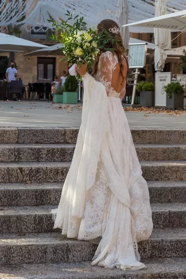 Frau in weißem rückenfreiem Brautkleid mit Blumenstrauß steht auf einer Treppe auf Mallorca