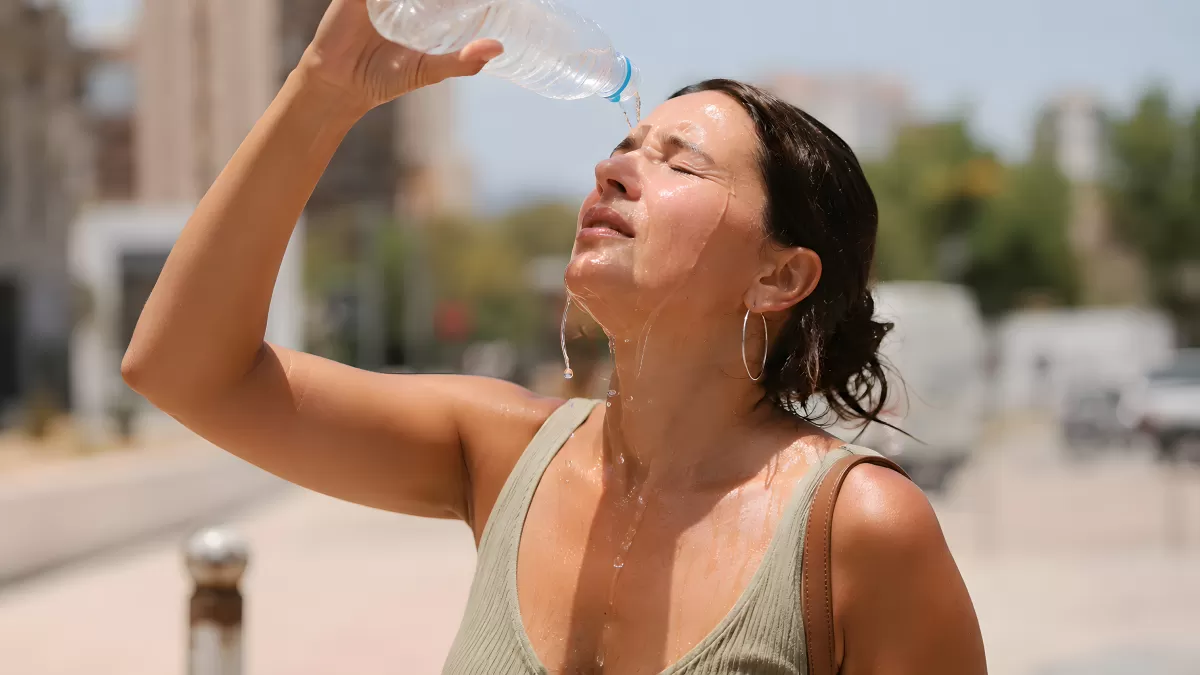 Frau kühlt sich bei Hitze mit Wasserflasche ab