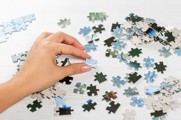 Frau löst ein Puzzle mit vielen Puzzleteilen, auf einem weißen Holztisch