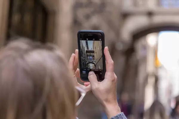 Frau macht ein Handyfoto der Touristenattraktion und mediterranem Skywalk "Pont Gòtic" in der Carrer del Bisbe in Barcelona, Spanien