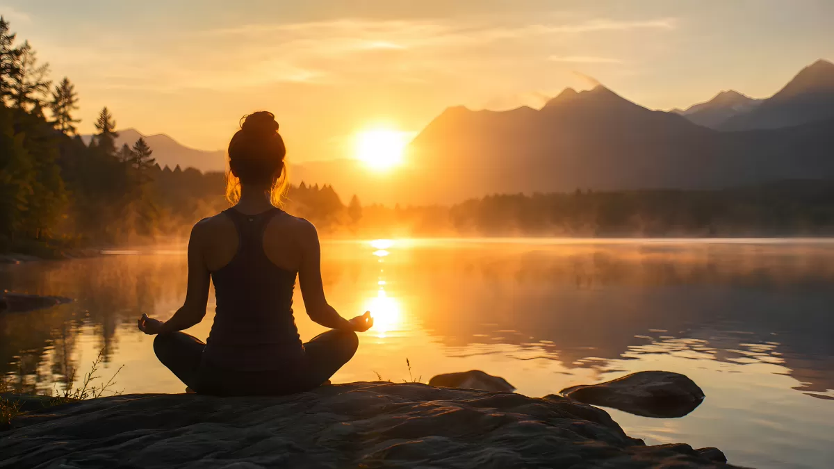 Frau meditiert im Lotussitz am See bei Sonnenaufgang