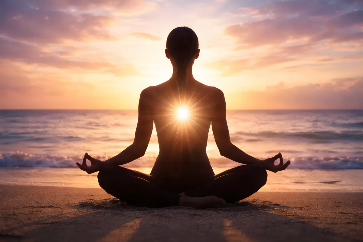 Frau meditiert im Lotussitz am Strand bei Sonnenuntergang
