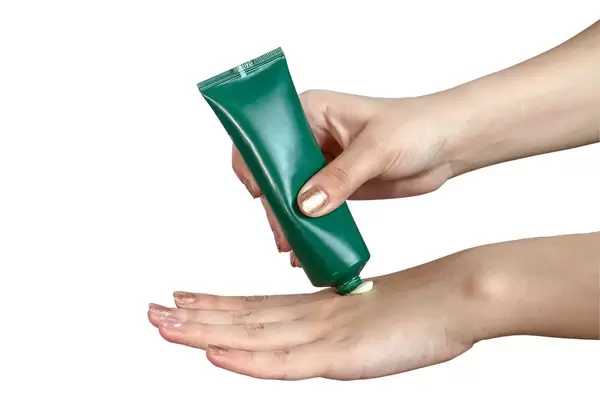 Frau pflegt ihre Hände und trägt Handcreme aus grüner Tube auf vor weißem Hintergrund