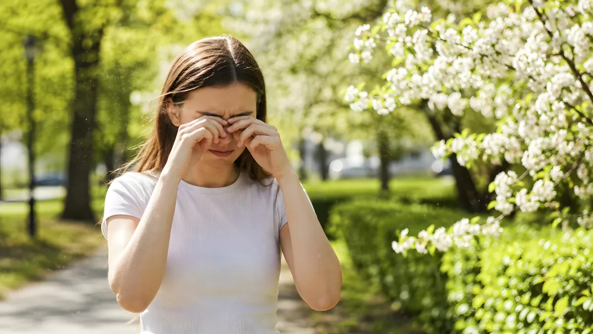 Frau reibt sich die Augen bei Pollenflug im Park