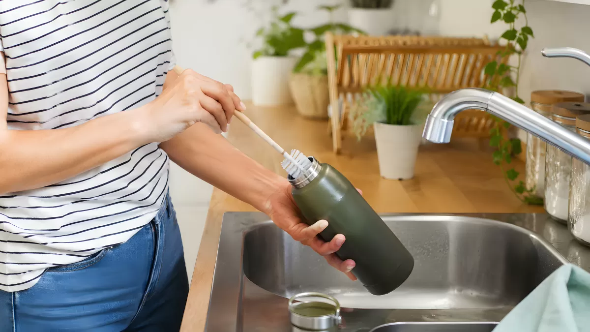 Frau reinigt Thermosflasche mit Flaschenbürste am Spülbecken
