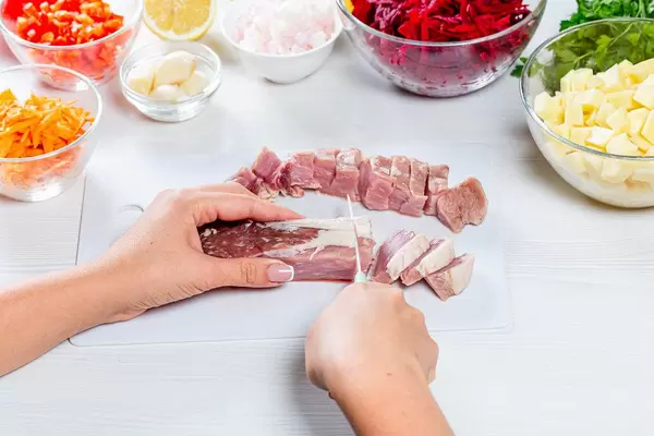 Frau schneidet Schweinefleisch auf einem Küchentisch