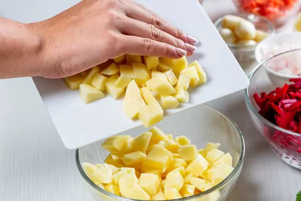 Frau schüttet für den Kochprozess geschnittene Kartoffelstücke in eine Glasschale