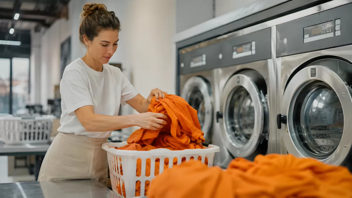Frau sortiert orangefarbene Wäsche im Waschsalon