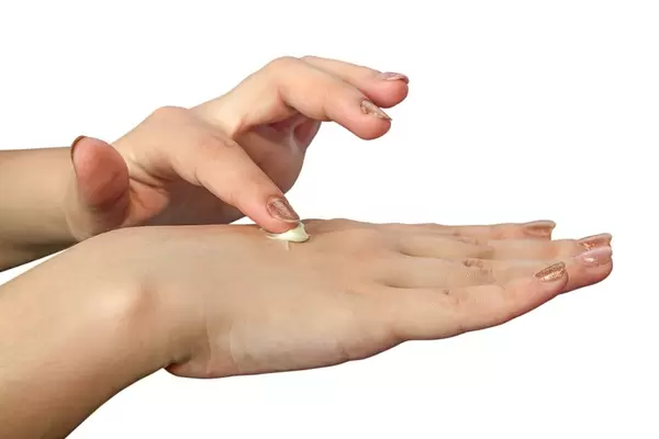 Frau trägt Handcreme auf Handrücken auf vor weißem Hintergrund