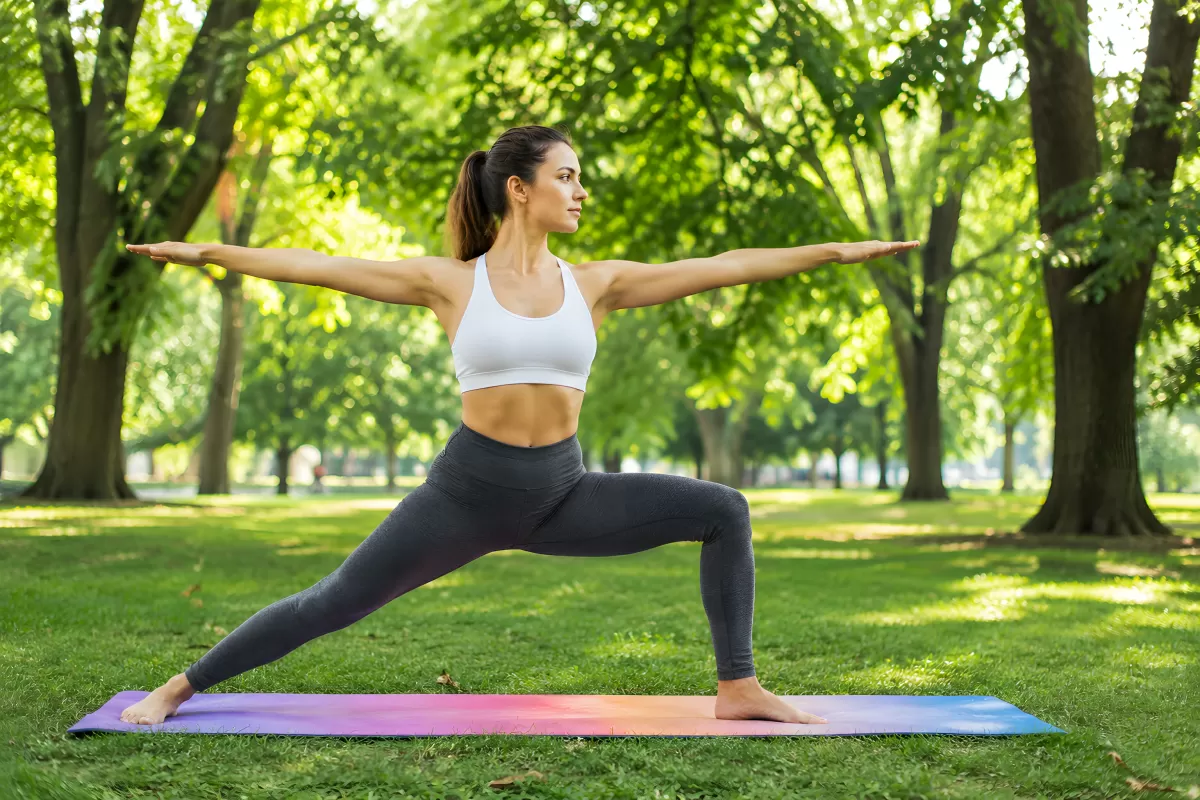 Frau übt Krieger-Pose auf bunter Yogamatte im Park