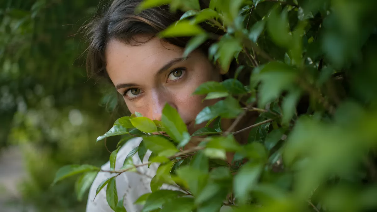 Frau versteckt sich lächelnd hinter grünem Blattwerk