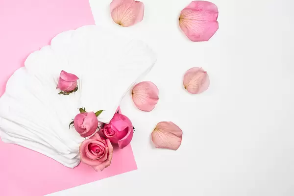 Frauen-Hygieneartikel: lose Slipeinlagen und Rosen auf rosa-weißem Hintergrund mit Platz für Text