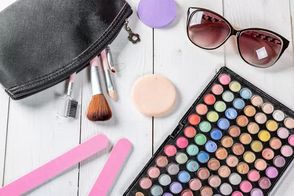 Frauen-Kosmetik auf einem weißen Holztisch - Sonnenbrille, Schminkpallete, Pinsel und Make-Up-Pads