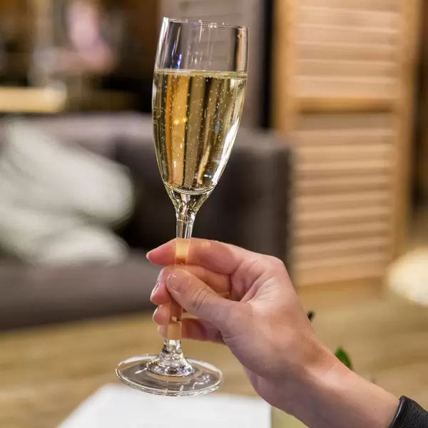 Frauenhand hält sprudelnden Sekt im Glas vor unscharfem Hintergrund in der The Corner Bar in Barcelona, Spanien