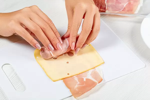 Frauenhand rollt Würstchen in Käse und Schinken ein