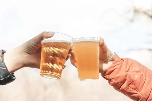 Frauenhänden mit Bier in Plastikbechern anstoßen vor Himmel-Hintergrund