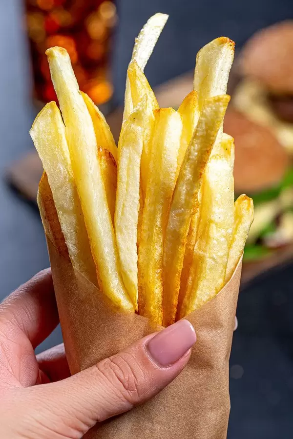 French fries in a paper wrapper in a woman's hand close up