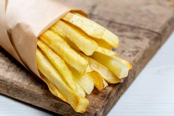 French fries in a paper wrapper on wooden board