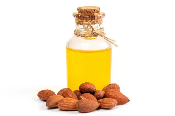 Fresh almonds with bottle of oil over white background