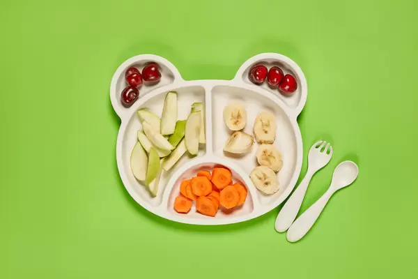 Fresh cherries, apple, banana and carrot slices on bear-shaped bamboo plate