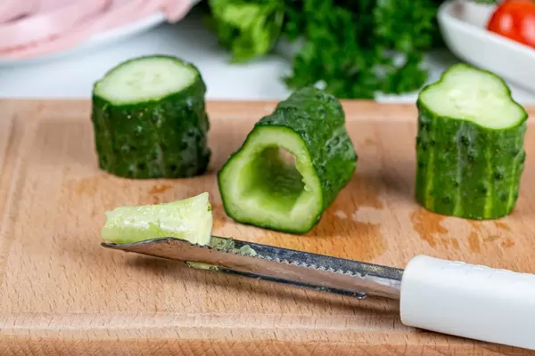 Fresh cucumber slices and knife on wooden kitchen board