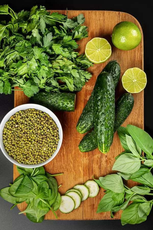 Fresh cucumber, spinach, basil, green peas, parsley, lime on wooden board, top view