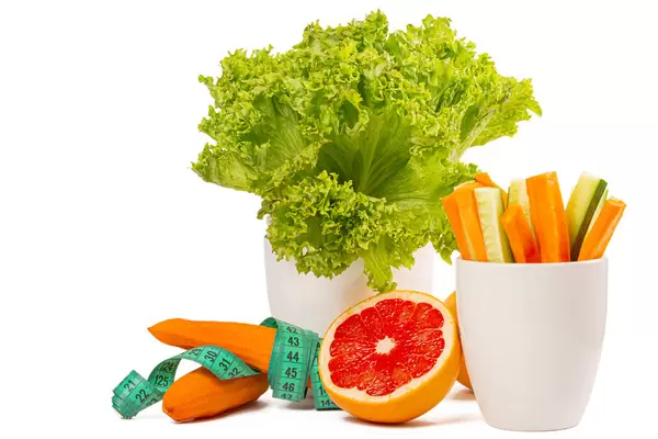 Fresh diet vegetables and half grapefruit on white background with measuring tape