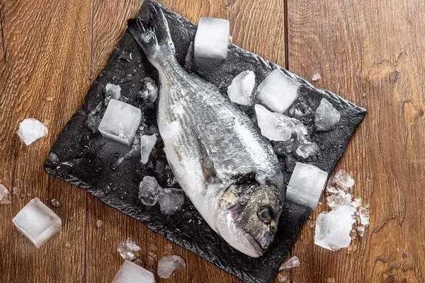Fresh Dorado fish with ice cubes on wooden table (Flip 2019)
