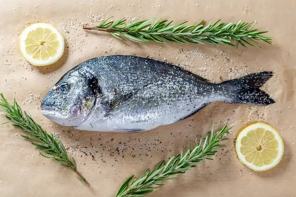 Fresh Dorado fish with lemon slices, spices and fresh rosemary on parchment