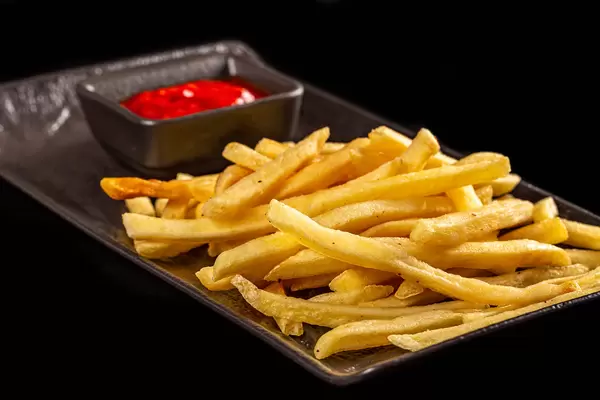 Fresh french fries and tomato sauce on a black background, close-up