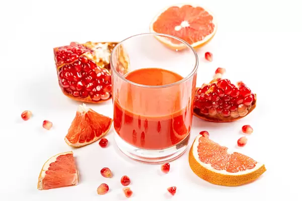 Fresh fruit grapefruit and pomegranate with a glass of juice on a white background