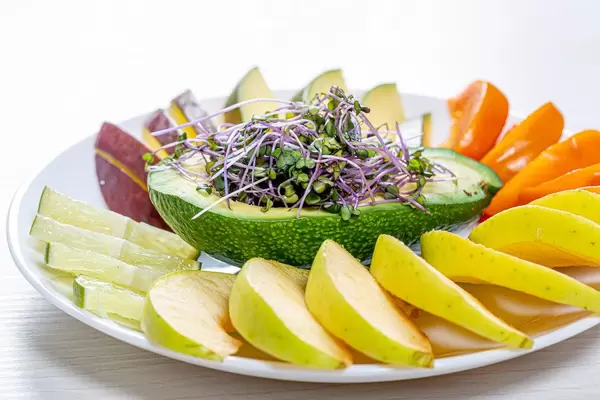 Fresh fruit slicing on a white plate with avocado and micro green cabbage