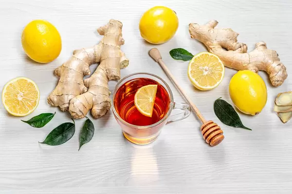 Fresh ginger roots, lemons and green leaves with a Cup of tea on a white wooden background