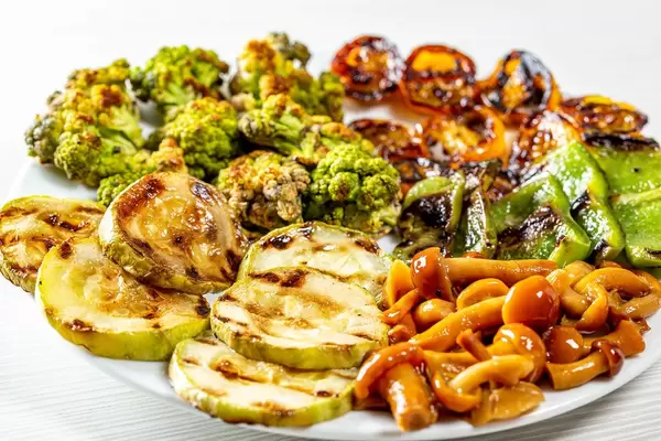 Fresh grilled vegetables and pickled mushrooms on a white plate
