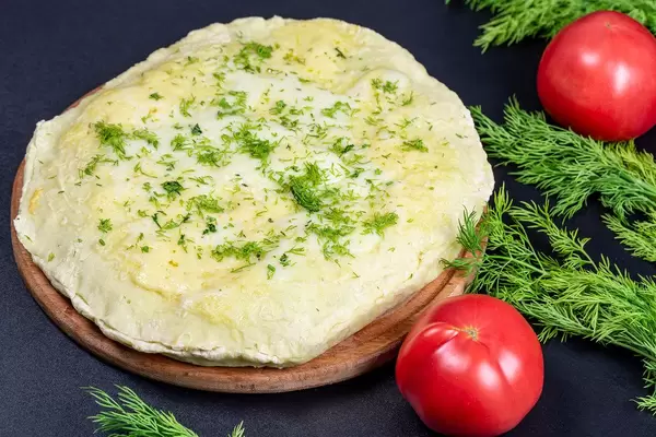 Fresh homemade khachapuri with cheese and minced meat on a black background with dill and tomatoes