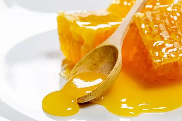 Fresh honey pours from a wooden spoon and honeycomb