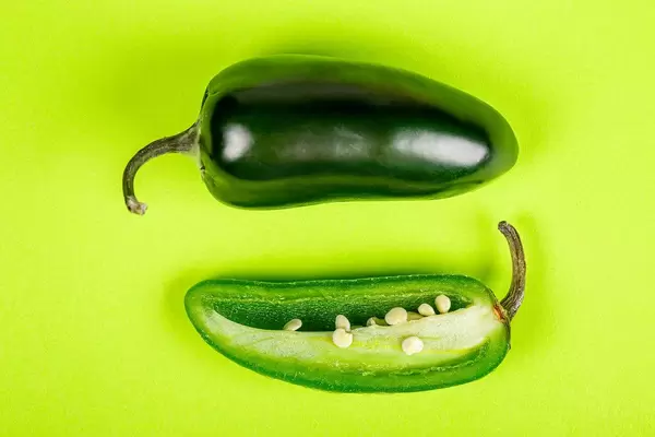 Fresh hot jalapeno pepper on a green background, top view