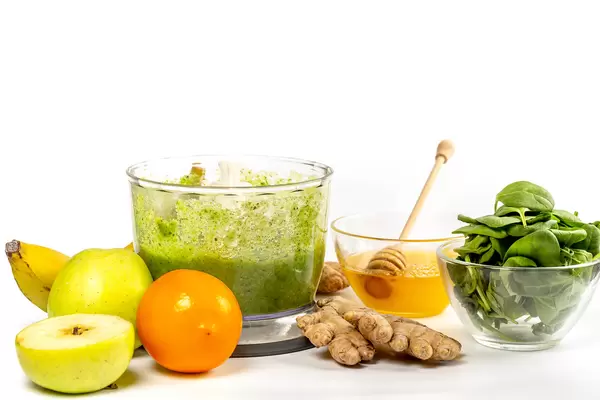 Fresh ingredients - lemon, apple, banana, honey, ginger and spinach on white with ready-made smoothie in blendew