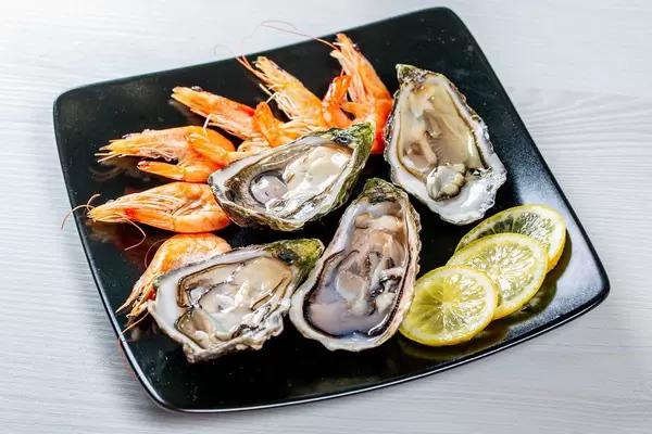 Fresh large oysters and shrimp with lemon slices in a black plate