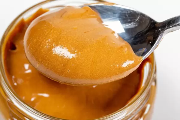 Fresh made creamy peanut butter in a glass jar with spoon