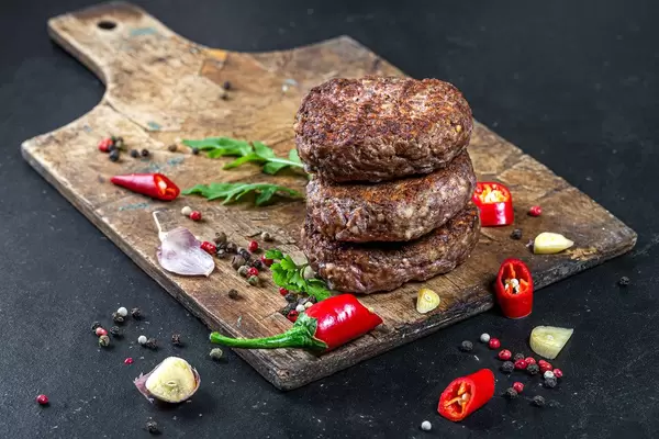 Fresh meat cutlets with spices, pieces of chili and garlic on an old kitchen Board (Flip 2019)
