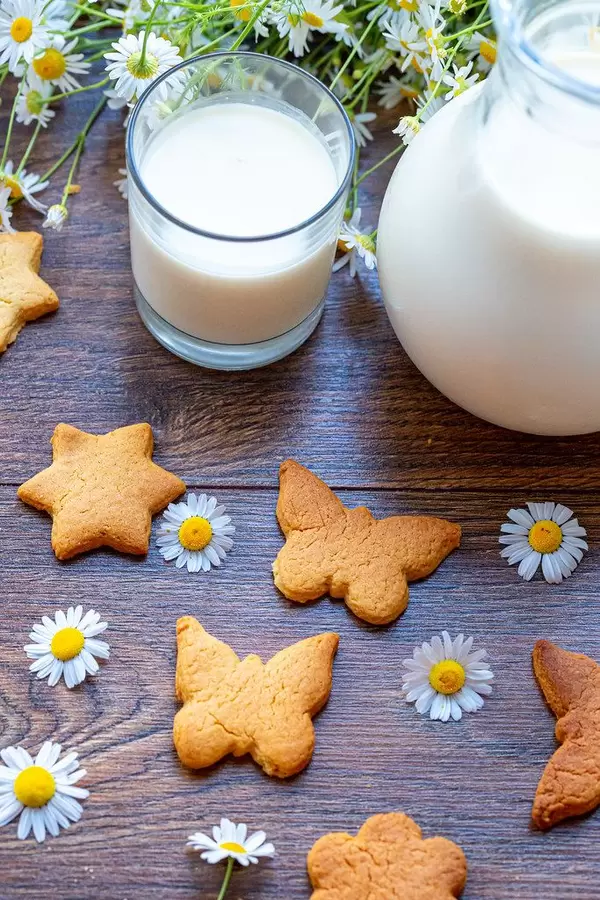 Fresh milk, homemade cookies and daisies on wooden background