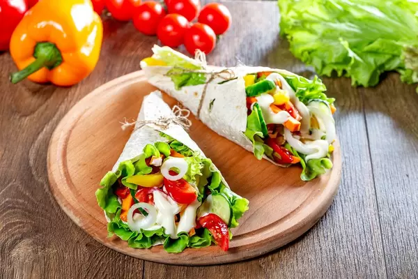 Fresh multi-colored sliced vegetables wrapped in pita bread on the kitchen Board (Flip 2019)