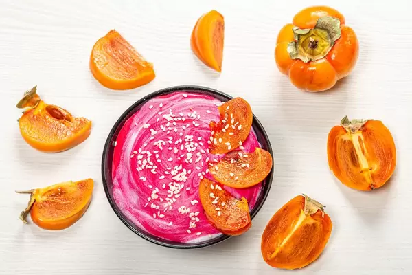 Fresh oatmeal with pink yogurt, sesame seeds and fresh persimmons on a white background. Top view (Flip 2019)