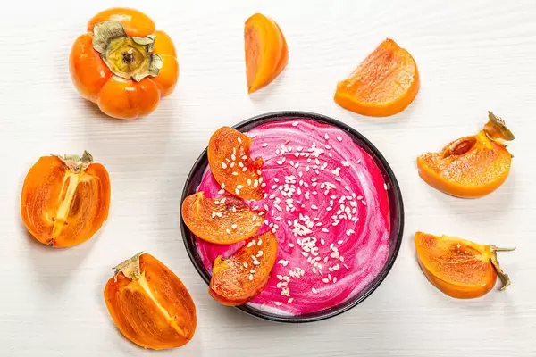 Fresh oatmeal with pink yogurt, sesame seeds and fresh persimmons on a white background. Top view